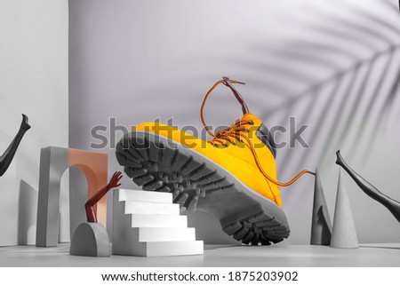Shoe concept, yellow boots on the stairs, women's legs and hands, palm shade on gray background, arch and other geometric shapes, color 2021