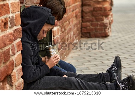 two homeless kids counting money given by strangers, beggars sit on the ground begging, side view