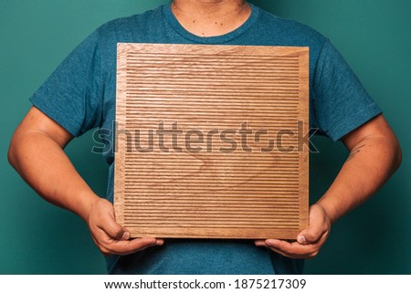 Hispanic male holding a wooden letterboard with empty space to add quotes, messages or a sign.