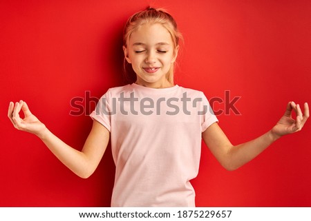 calm beautiful little girl stand meditating in studio, engaged in yoga. attractive girl in t-shirt stand with eyes closed, keep calm, concentrated