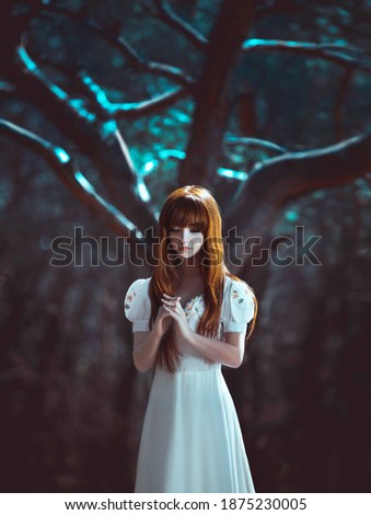 Young beautiful red-haired lady girl, stands in mystical dark deep dense forest hands folded in prayer. Night background, wood tree moon light. White long vintage dress. Scared medieval princess girl