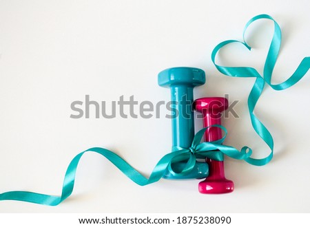 Two turquoise and pink dumbbells with ribbon bow on white background with copy space. Concept Valentines day, male and female, healthy lifestyle, giving gifts, love of sports. Trendy color green tide.