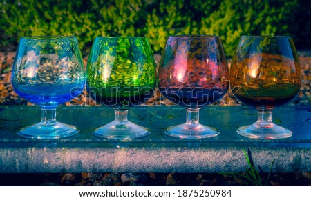 A selection of colourful brandy or liqueur glasses in a row on a granite slab in a lush garden