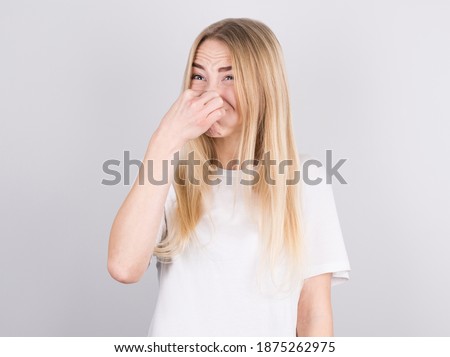 Young woman with disgust on his face pinches nose on white background. Negative emotion facial expression.