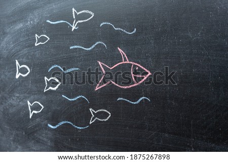 The concept of leadership and teamwork. Red fish on a chalk Board