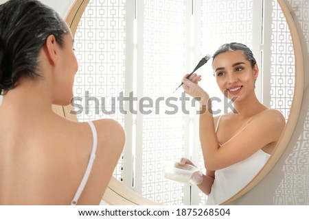 Young woman applying dye on hairs near mirror indoors Royalty-Free Stock Photo #1875268504