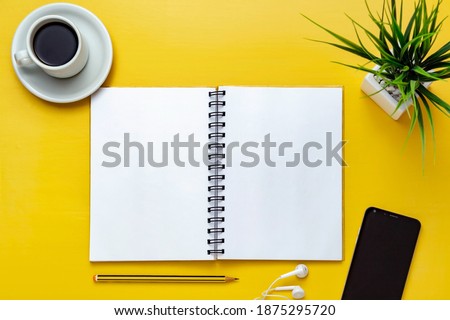 Notebook mockup on yellow office desk. Top view. Isolated blank sheet for design, list, script, text, draw, annotations and creativity. Pencil, cup of coffee cell phone, headphones and plant beside.