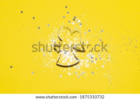 silver Christmas themed cookie cutter on a bright yellow background with silver glitter and star confetti