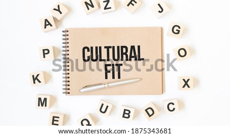 Text CULTURAL FIT on the craft colored notepad with block wood cubes on the white background