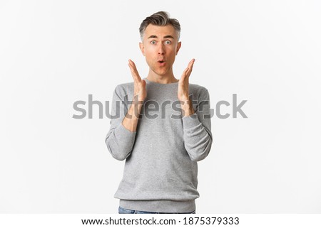 Image of middle-aged man with gray short hair, looking amazed and fascinated, saying wow, reacting to advertisement, standing over white background