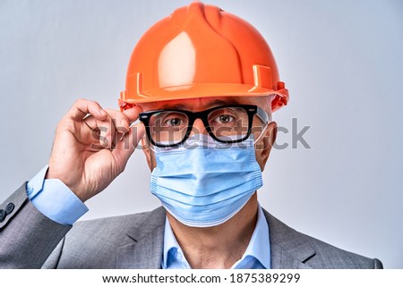 Close up of mature man wearing a protective mask and adjusting glasses, isolated on blue background. Protection and safety concept