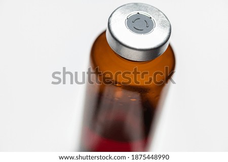A macro shot with selective focus of an amber color vaccine injection bottle set on plain white background.