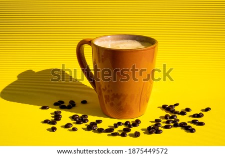 Exquisite freshly made sparkling coffee inside a brown cup with coffee beans scattered on a yellow table with a yellow background reflecting a black shadow on the side.