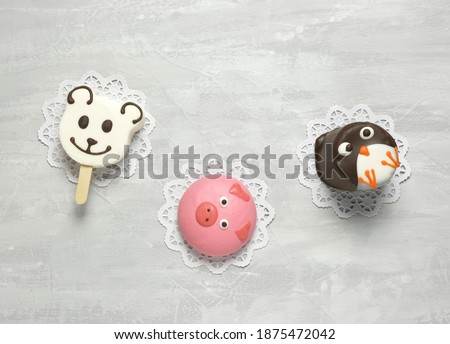 Children's figure cookies in the shape of a penguin, a piglet and a bear are covered with multi-colored glaze. Top view on a concrete background with empty space for text. Selective focus