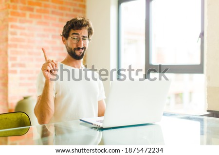 young bearded man with a laptop feeling like a genius holding finger proudly up in the air after realizing a great idea, saying eureka Royalty-Free Stock Photo #1875472234