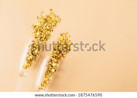 Glasses with golden confetti tinsel on beige background. Flat lay, top view, copy space. Celebrate party concept.