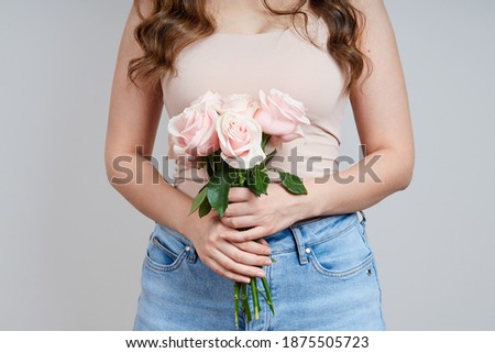 Portrait of a beautiful headless woman in a pink T-shirt, jeans with a bouquet of pink roses. Studio shot on gray background. Holiday concept of valentine's day, birthday, mother's day, womens day.