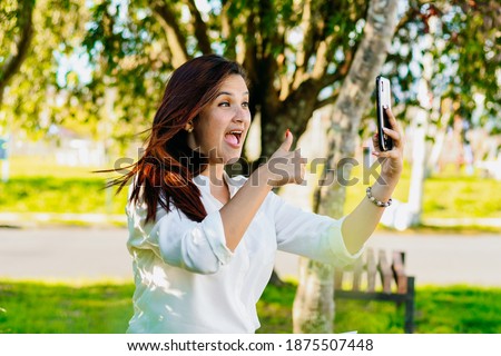 Executive woman making a video call, sitting in the park. Making a sign of everything well with her hand.
