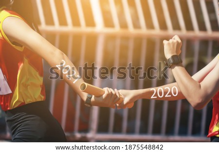 Professional Athlete passing a baton to the partner against race on racetrack.between 2020 and 2021 years.happy new year 2021.