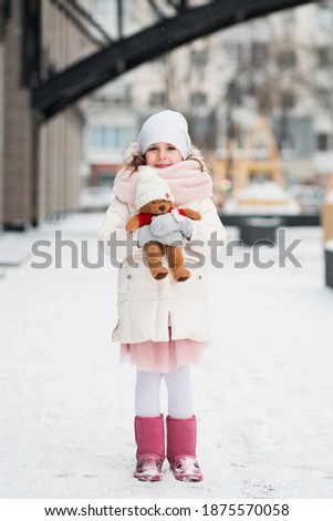 Happy little girl standing in winter city with teddy bear.