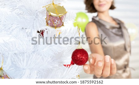 Caucasian adult woman soft touch red ball ornament that hanging on white pine tree by her finger after decoration design for invitation friends coming home in Happy Christmas Eve party