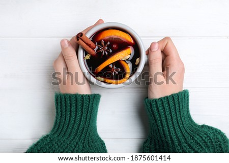 Woman with cup of mulled wine at white wooden table, top view