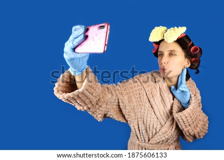 Young housewife girl with curlers on head takes a selfie on phone