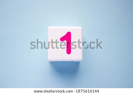 Close-up photo of a white plastic cube with a pink number one on a blue background. Object in the center of the photo Royalty-Free Stock Photo #1875616144