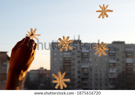 A woman's hand draws snowflakes on the window with paint, everything is illuminated by a soft yellow sunset light, close-up, copy space. Preparing for Christmas and New Year, home decoration