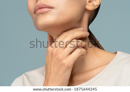 Closeup of sick woman having sore throat, tonsillitis, feeling sick, caught cold, suffering from painful swallowing, strong pain in throat, holding hand on her neck, isolated on studio blue background Royalty-Free Stock Photo #1875644245