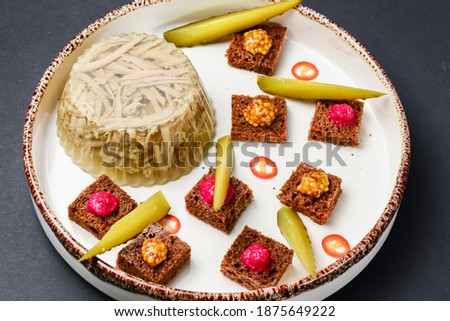 Beef tongue on a white plate, meat-in-jelly with bread with sauces and pickles. Over black background.