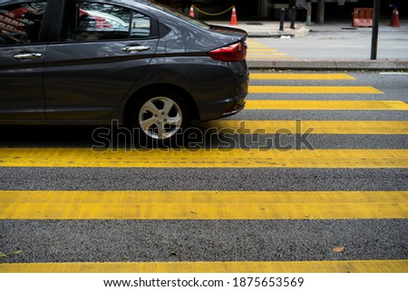 Cars and motorcycles are passing through the pedestrian crossing. Yellow stripes of the crosswalk.