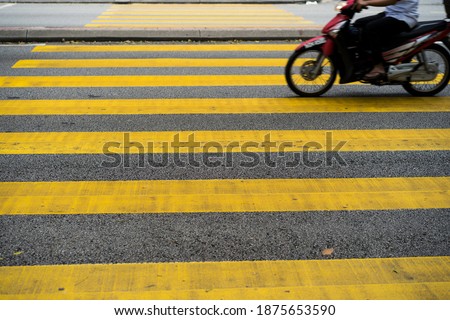 Cars and motorcycles are passing through the pedestrian crossing. Yellow stripes of the crosswalk.
