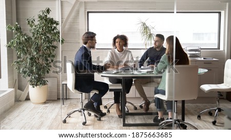 Diverse international businesspeople sit at desk in office boardroom talk discuss ideas together. Multiracial colleagues brainstorm at team group business meeting or briefing. Cooperation concept.
