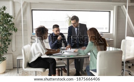 Multiracial businesspeople talk brainstorm discuss company financial statistics document at team meeting in office. Motivated multiethnic colleagues gather in boardroom consider paperwork at briefing. Royalty-Free Stock Photo #1875666406