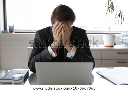 Upset male boss or CEO sit at desk in office feel distressed frustrated with bad online news message on computer. Unhappy businessman work on laptop depressed with business failure or project loss. Royalty-Free Stock Photo #1875669865