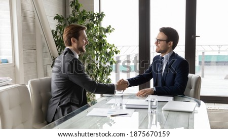 Wide panoramic view of successful young businessmen shake hands closing deal or making agreement at meeting in office. Smiling male colleagues partners handshake get acquainted at business briefing.