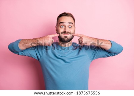 Photo of cute funny young man dressed blue sweater fooling pointing cheeks isolated pink color background