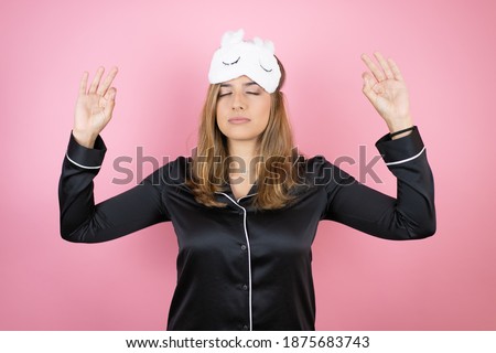Young caucasian woman wearing sleep mask and pajamas over isolated pink background relax and smiling with eyes closed doing meditation gesture with fingers