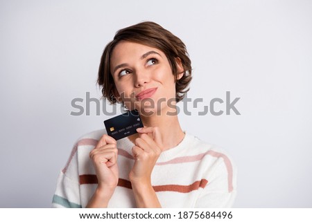 Photo of thoughtful young lady wear striped sweater holding bank card looking empty space isolated grey color background