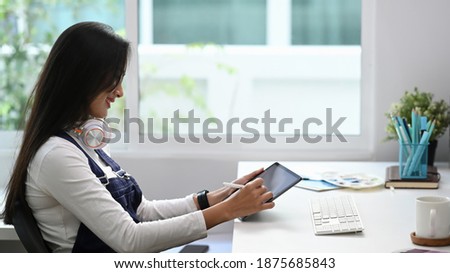 Side view of young female designer holding stylus pen and working on digital tablet.