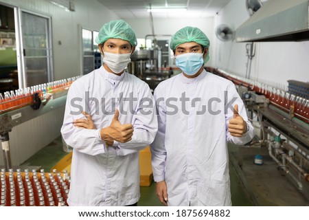 portrait couple of asian male factory worker wearing medical mask and thumbs up post in beverage factory