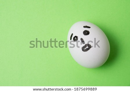 An egg with a surprised face, on a green background with copy space.