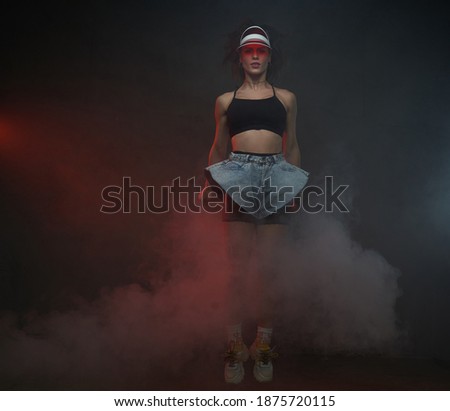 Beautiful female dancer in short cloth ing with red cap jumps in dark background posing in air.