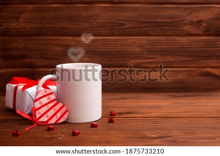 Cup of tea or coffee with steam and gift box in one heart shape on wooden background. Valentine's day celebration greeting card or love concept. Copy space
