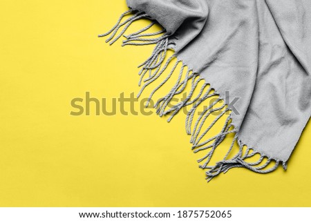 Trending colors of 2021 Ultimate Gray and Illuminating. Grey scarf with tassels on yellow background. Minimal winter or autumn background for your design.