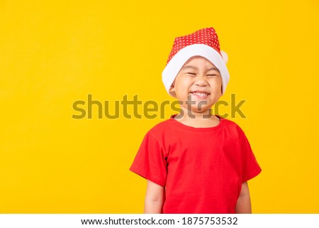 Kid dressed in red Santa Claus hat, Portrait of Asian little cute boy smile and excited the concept of holiday Christmas Xmas day or Happy new year, studio shot isolated on yellow background