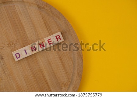 Dinner menu concept. Scrabble letter tiles on wooden table. Yellow background.