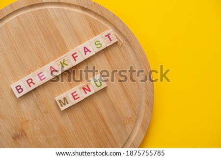 Breakfast menu concept. Scrabble letter tiles on wooden table. Yellow background.