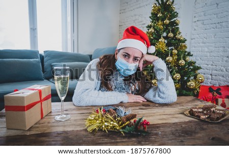 Sad woman with mask home alone in self isolation at christmas feeling depressed mourning and missing family and friends. COVID-19 Lockdown and quarantine during winter holidays and mental health.